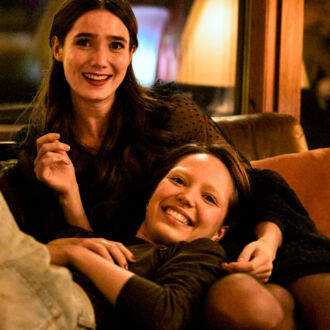 Three teenage girls are smiling on a sofa.