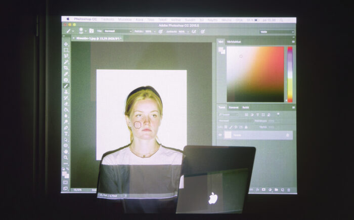 On voit une projection élargie d'un écran d'ordinateur sur lequel un programme informatique de type Photoshop fait apparaître un visage féminin éclairé, l’impression qui s’impose étant que le sujet est partie intégrante de l'écran. 
