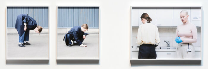 Trois photos présentées sur un mur montrent deux femmes dans la rue ainsi que dans une cafétéria, occupées à ramasser quelque chose qui se trouve au sol ou devant elles. 