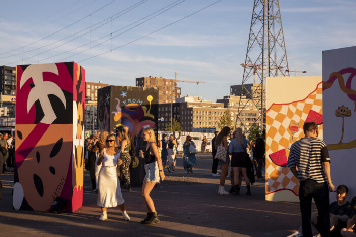 People look at artworks that are painted on upright rectangular boxes several metres high.