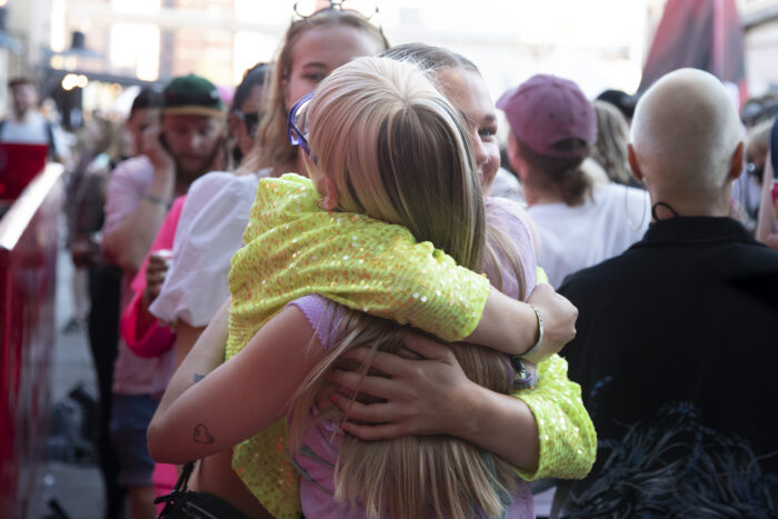 Two people are hugging in the foreground, among a crowd of concertgoers.