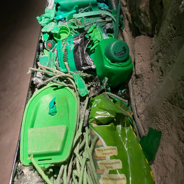Teile von Plastikmüll, ganz grün, darunter ein Spielzeugboot, Bonbonpapier und ein Flaschenverschluss.