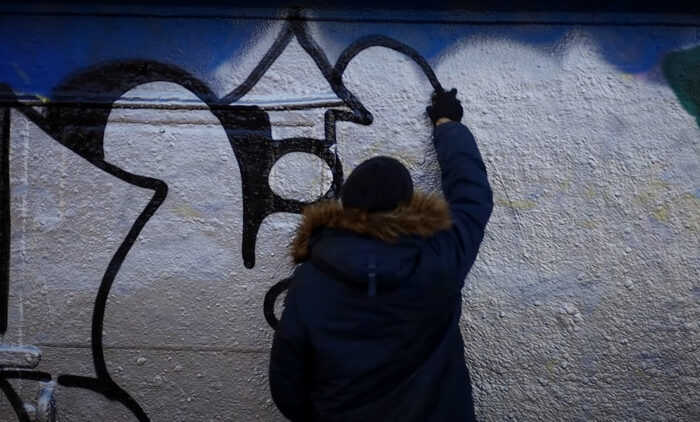 Um homem está pintando um desenho na parede, de costas para a câmera.