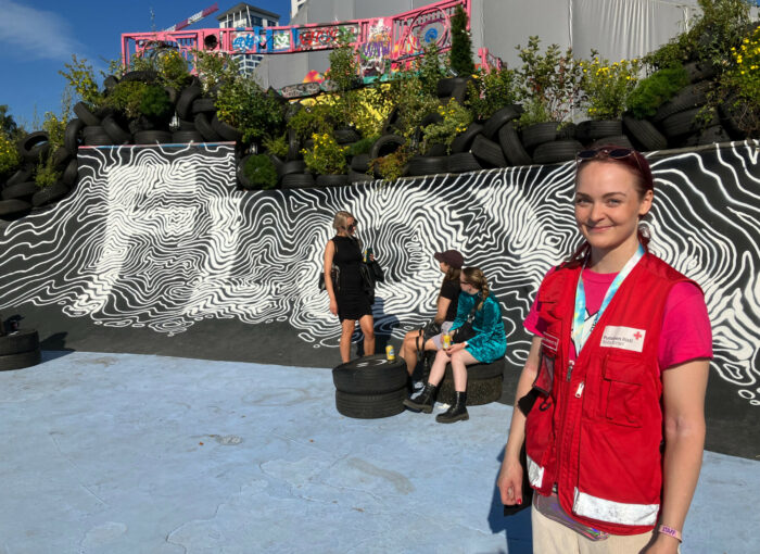 A woman in a red vest stands in front of a wall painted with the word Flow.