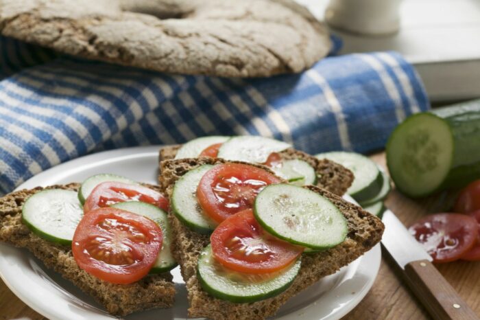 Pedaços de pão de centeio cortados de um pão redondo e achatado são cobertos com fatias de pepino e tomate.