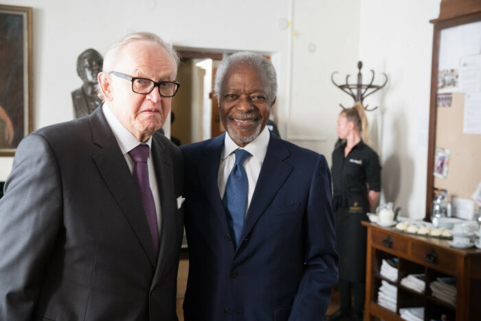 A white man and a black man, both dressed in suits and ties, smile at the camera.