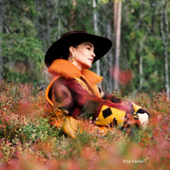 Una mujer con sombrero de ala ancha posa sentada en el claro de un bosque.