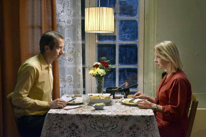 Um homem e uma mulher estão sentados frente a frente em uma pequena mesa, comendo uma refeição.