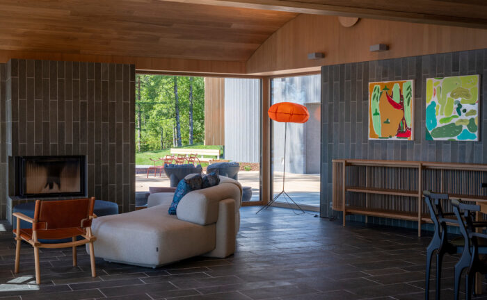 A área de estar inclui cadeiras, sofá, lareira, pinturas nas paredes e janelas amplas.