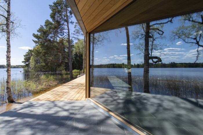 A lake view is reflected in the large window of a shoreline building.