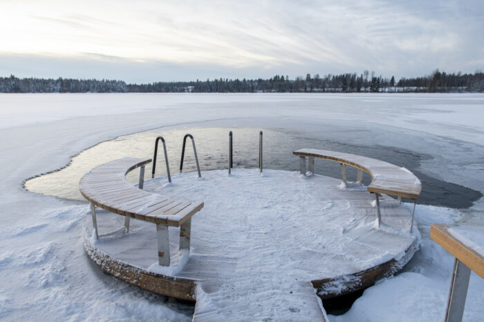 A round, snow-covered dock juts out into a mostly frozen lake.