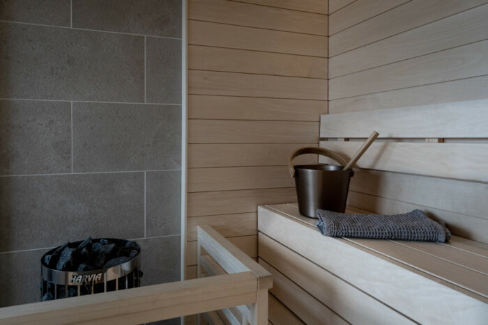 A wooden sauna bench holds a bucket and a folded towel.