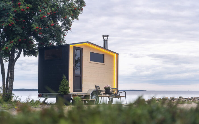 Uma pequena cabana de madeira sobre um trailer com rodas, estacionada na praia.