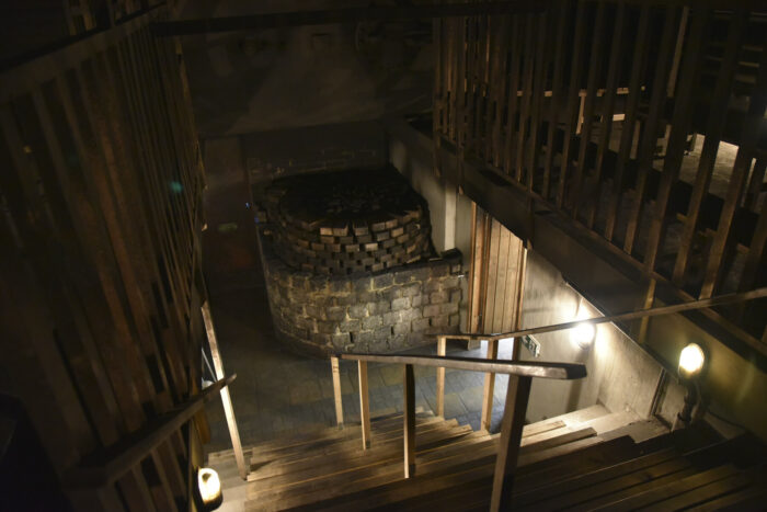 Dans un sauna de vastes dimensions, une galerie suspendue et un escalier surplombent un poêle géant en briques.