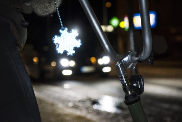 Numa estrada escura, o refletor de plástico em forma de floco de neve de um ciclista brilha quando um carro se aproxima.