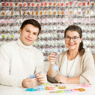 A man and a woman with small plastic reflectors in their hands are sitting at a table in front of a wall where rows of similar reflectors are hanging.