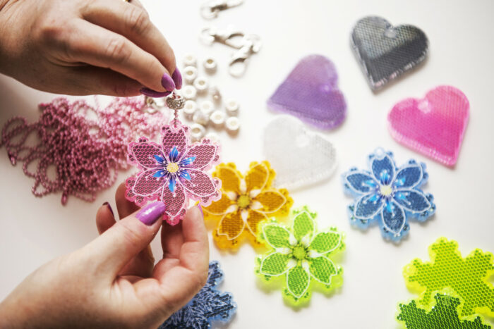 Two hands are holding a pink and blue snowflake-shaped plastic piece, with other shapes and colours lying on a table in the background.