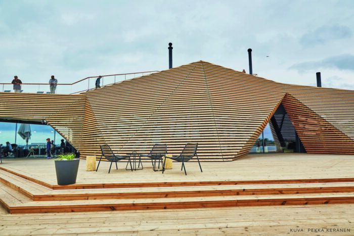 مجموعة كراسي في فناء خارجي لمبنى خشبي متعدد الزوايا بواجهة ذات ممر مثلث الشكل.