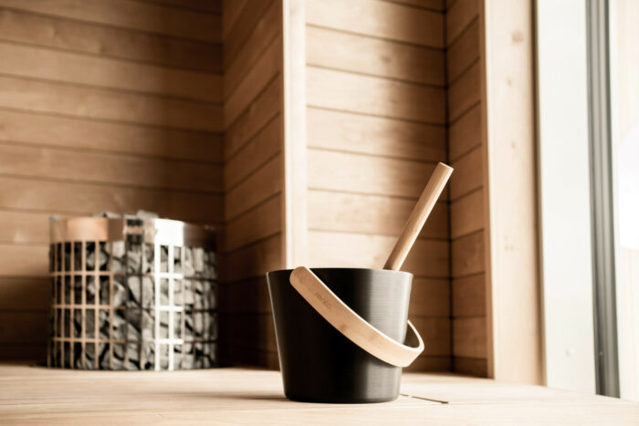 A wooden bucket is on a wooden bench in a sauna.