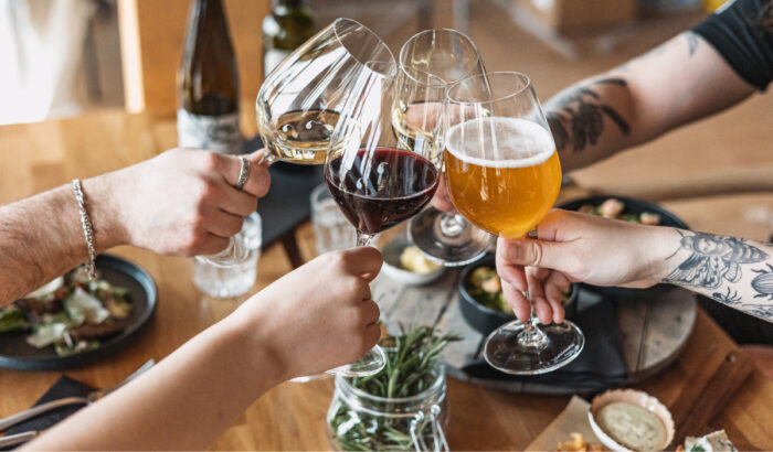 Over a table that contains a fine meal, four hands are clinking together the wineglasses they hold.