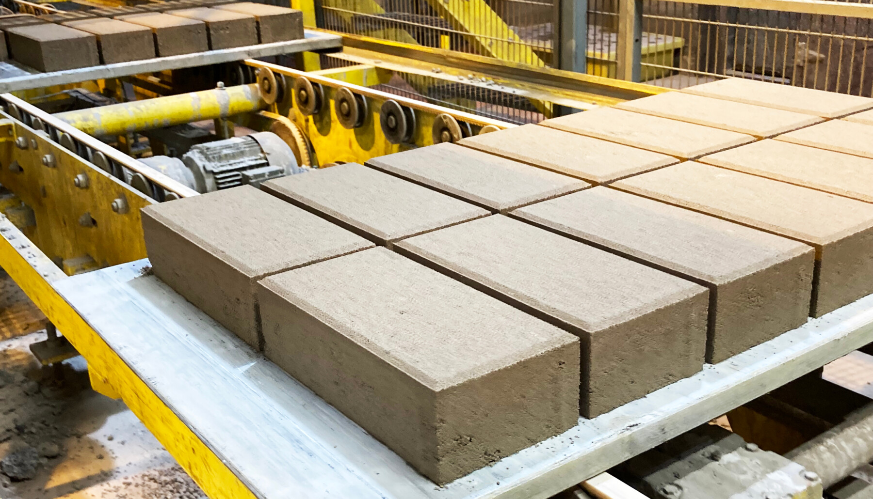 Dans une usine, plusieurs rangées de briques rectangulaires sont en train d’avancer sur la bande transporteuse d’une chaîne de production.