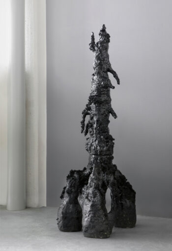 A black sculpture in the form of a tower with a three-pronged base.
