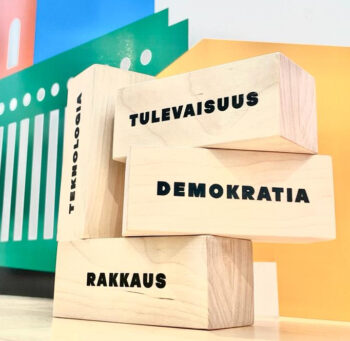 Quatre blocs miniature en bois sont empilés sur une table avec un mot différent inscrit sur chacun d’entre eux, à savoir futur, démocratie, amour et technologies. 