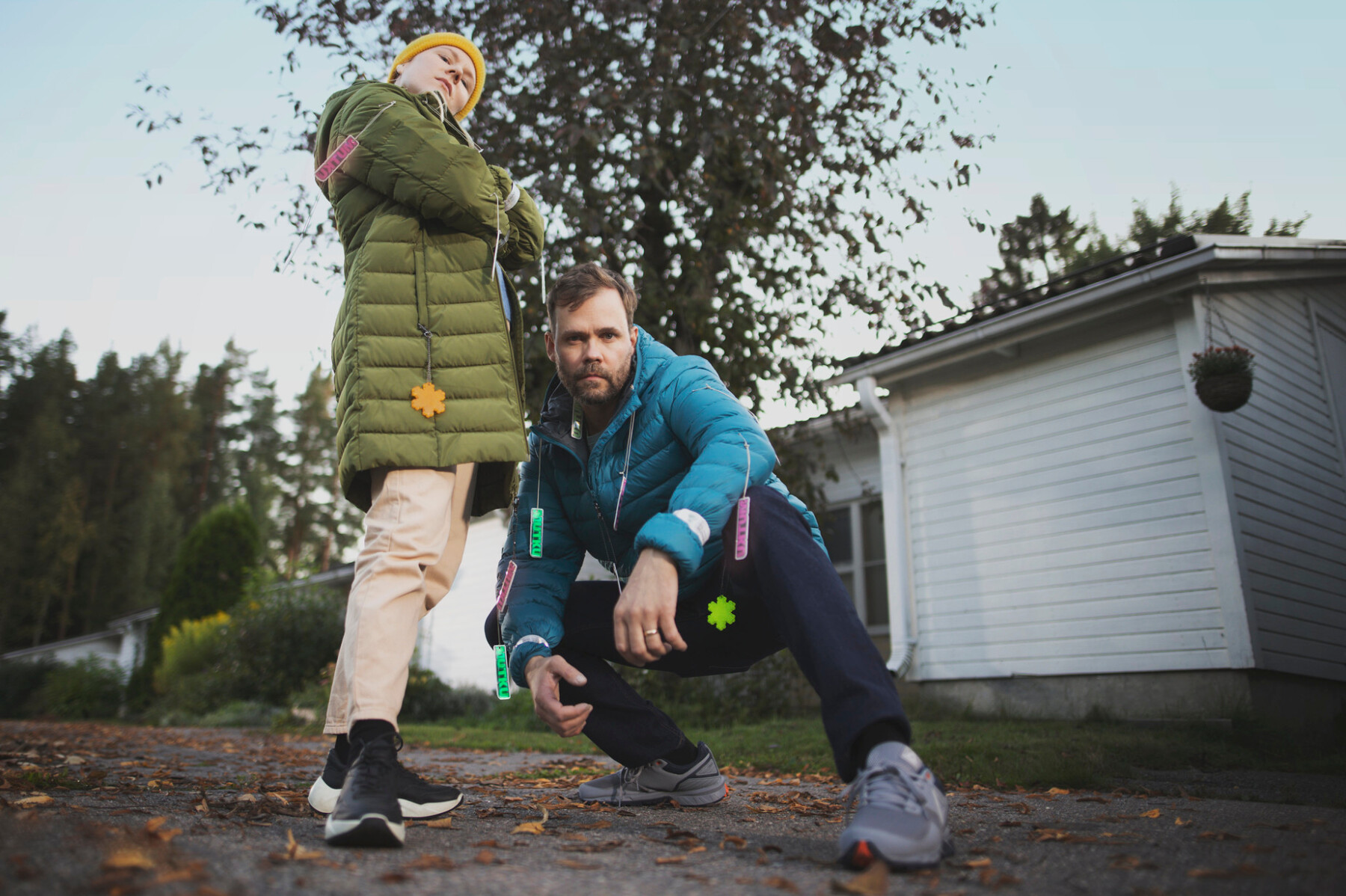 在一栋房子的院子里，一个男人和一个孩子穿着冬季外套，每人都佩带着几个塑料反光片，正在对着镜头摆姿势。