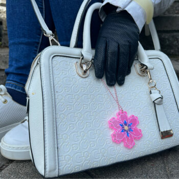 A pink, flat, six-pointed piece of plastic is attached to a white leather handbag.