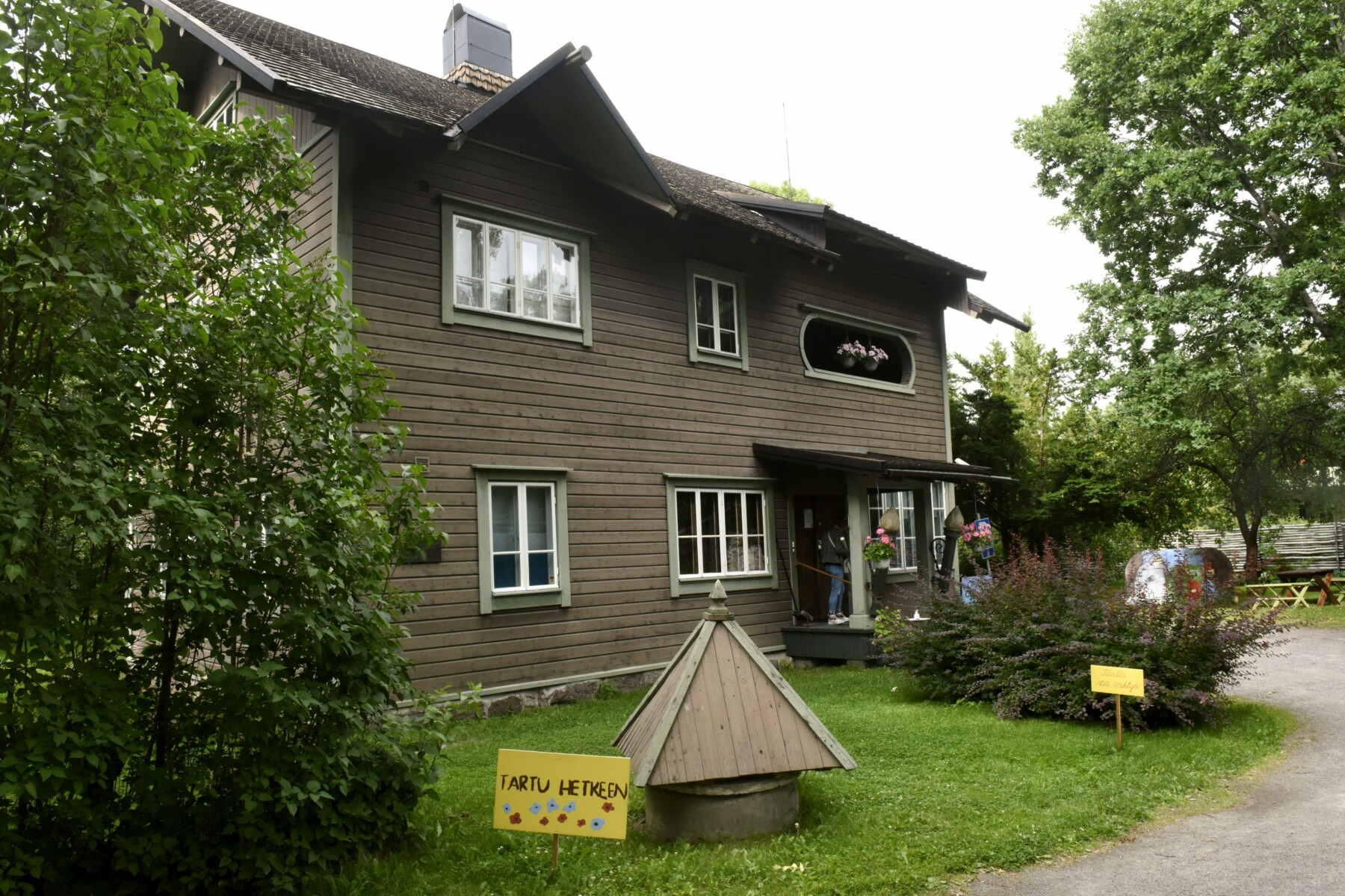 An old-fashioned brown wooden house is flanked by trees.