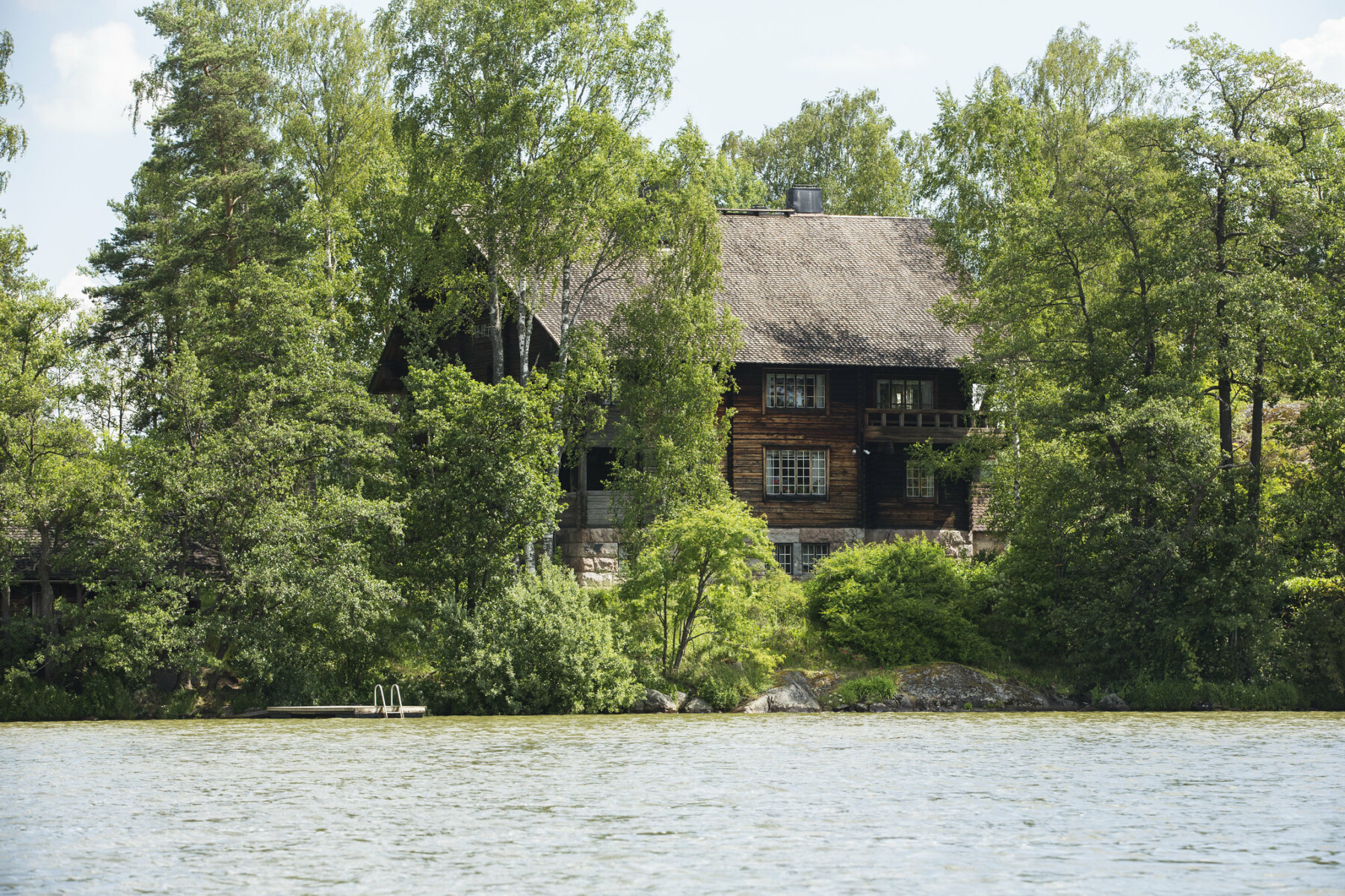 A view from the middle of a lake shows an expanse of water and a shoreline with trees and a brown wooden house.