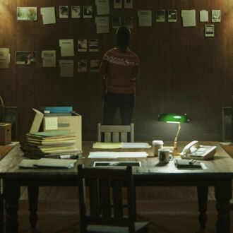 A realistic scene from a video game shows a wood-panelled room with books and papers piled on a table.