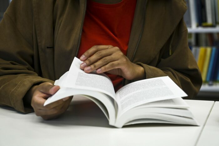 On voit les mains d’une personne en train de faire défiler les pages d’un livre posé sur une table.