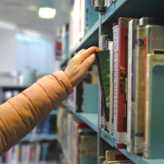 O braço de uma pessoa se estende para pegar um livro de uma estante.