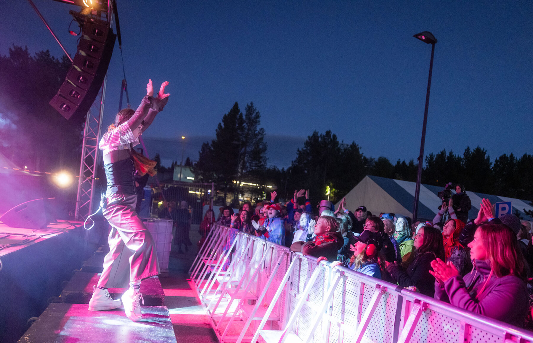 In dark twilight, a woman on an outdoor stage dances in front of an enthusiastic crowd of listeners.