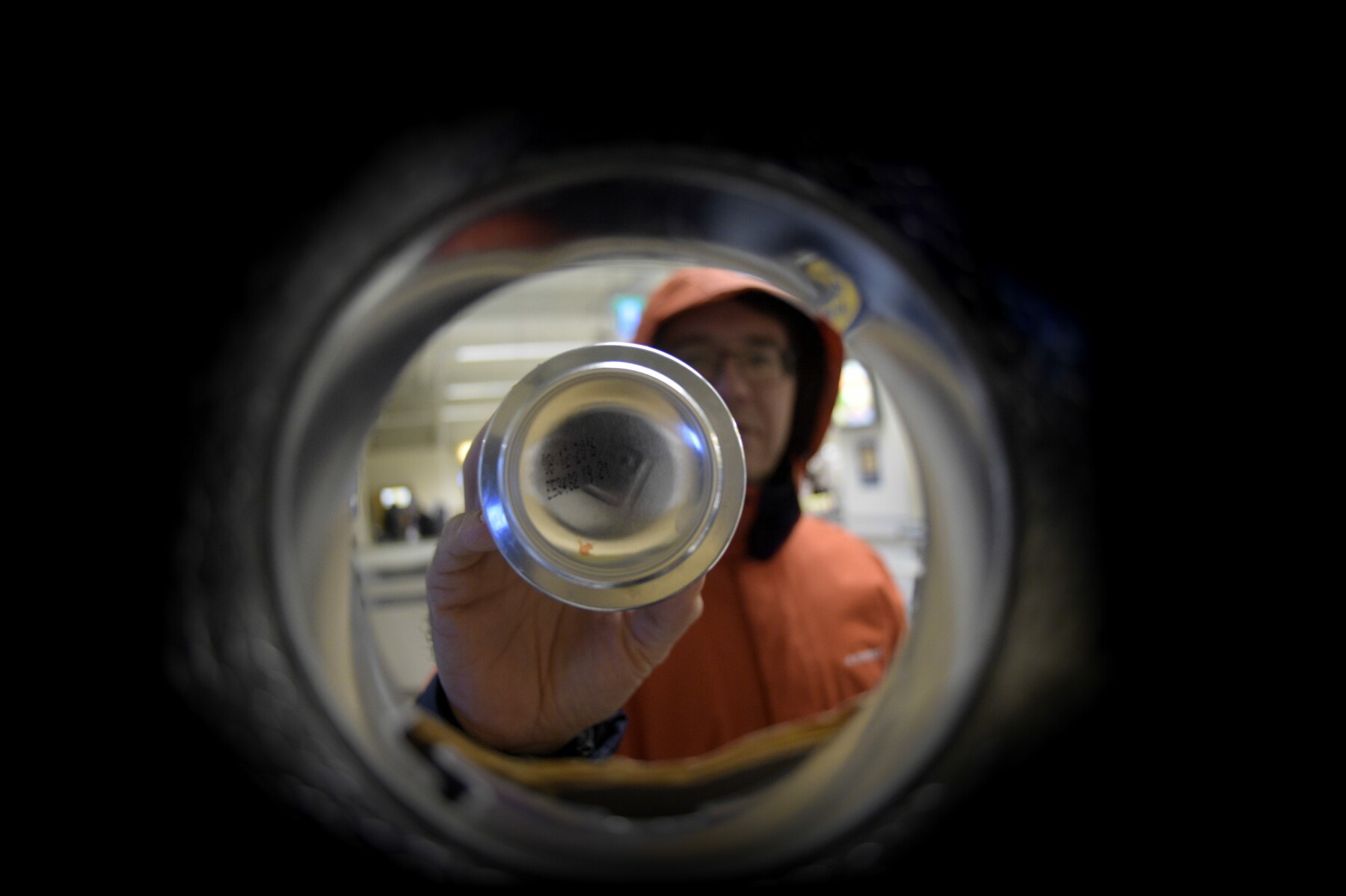 Une photo réalisée de l'intérieur d'une machine de consigne automatique de bouteilles montre une main en train d’introduire une bouteille dans la machine.