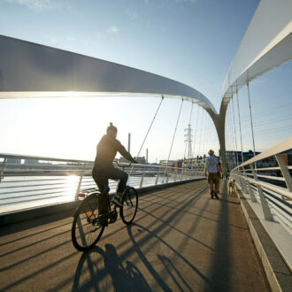 Una persona va en bicicleta por un puente y al fondo se ven el sol y el mar.