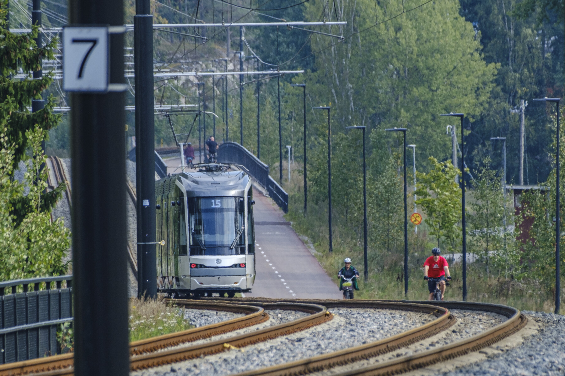 Un tramway circule sur ses rails tandis qu'à côté, des gens pédalent sur une piste cyclable.