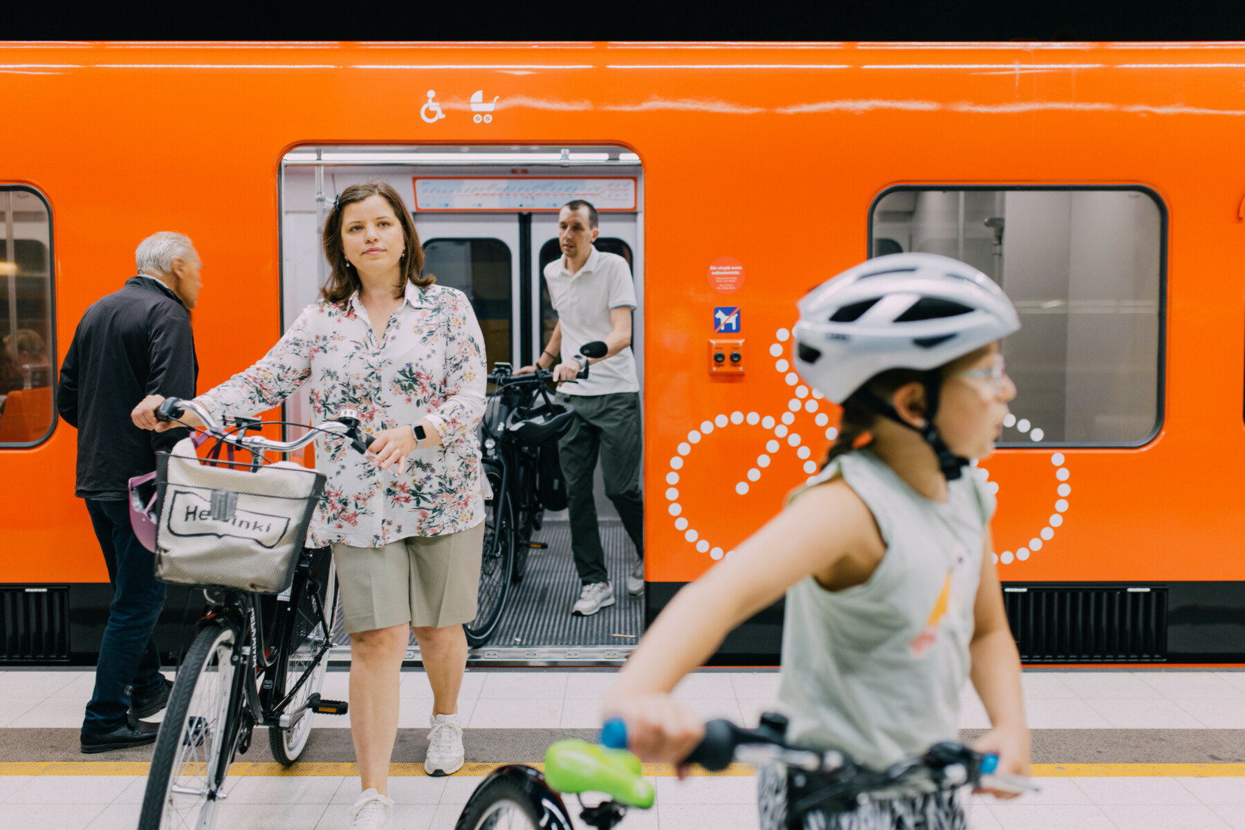 A man, a woman and a child are walking their bikes out of a metro train and onto the platform.