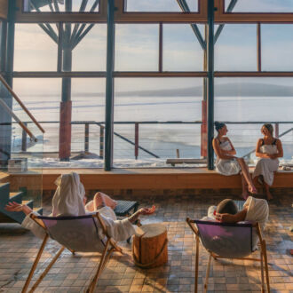 Several people in bathrobes lounge at a spa, with a wintery landscape visible through the windows.