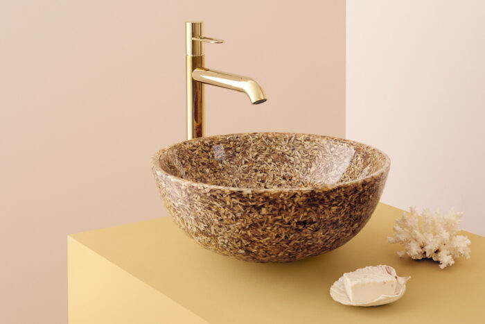 A round washbasin is on a countertop, under a faucet.