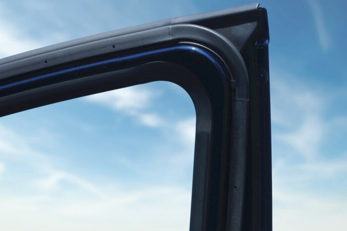 Part of a car door is viewed from the inside, set against the background of a blue sky.