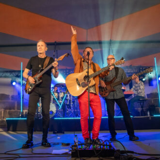 Tres hombres con guitarras actúan en el frente de un escenario.