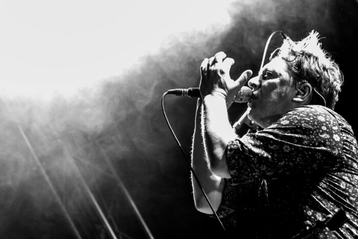 En la foto, en blanco y negro, un hombre canta ante un micrófono.