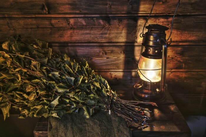 A lantern and a bouquet of leafy branches are on a bench in a wooden room.