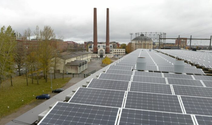 La photo présente des panneaux solaires sur le toit d’un bâtiment situé dans une zone industrielle. 