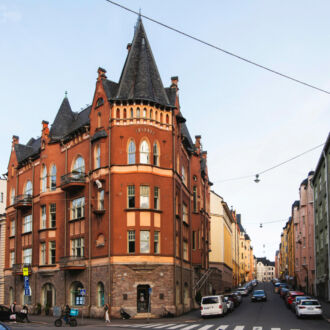 An impressive corner building featuring a tower and gables stands at the end of a street full of similarly ornate buildings.