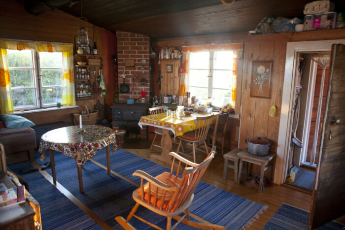 Interior of a cottage, with plenty of wooden furniture and several blue rugs.