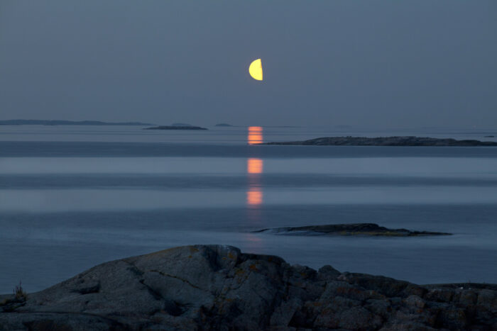 Moonlight is reflected in a dark sea between small islands.