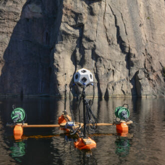 A research device on the surface of the water, with a rock wall in the background with prehistoric paintings.